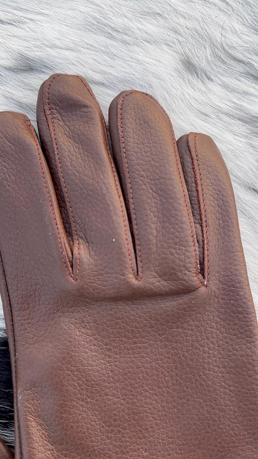 A single brown leather glove laid flat on a white faux-fur surface, showing the back of the hand with stitched finger separations and pebbled leather texture.