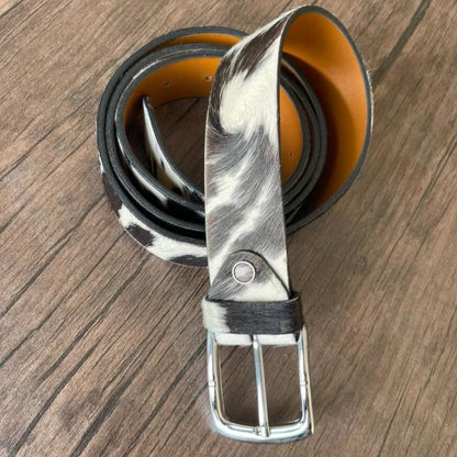 A rolled black and white cowhide belt with a silver buckle, displayed on a brown wooden surface.