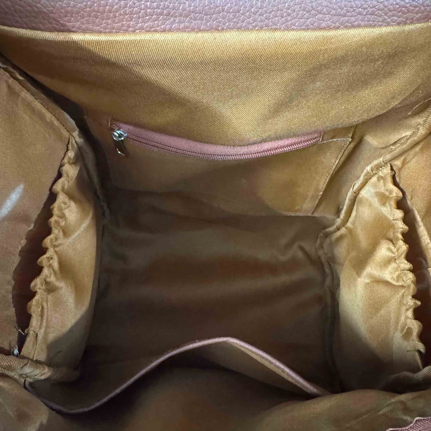 Close-up view of the interior of a handbag, showing a tan satin lining with a zippered pocket, elasticized side compartments, and a pinkish-brown textured leather exterior visible at the top.