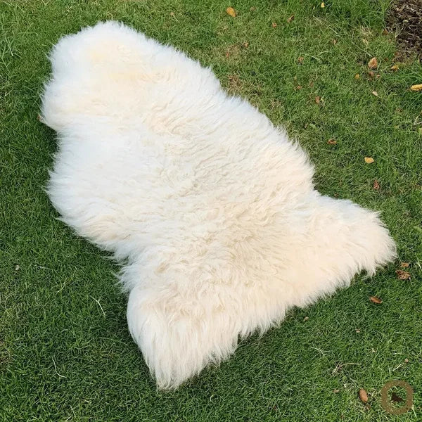 A fluffy white sheepskin rug laid out on green grass outdoors.