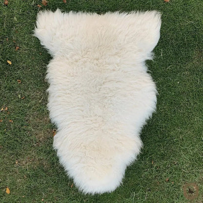 A fluffy white sheepskin rug laid flat on green grass.