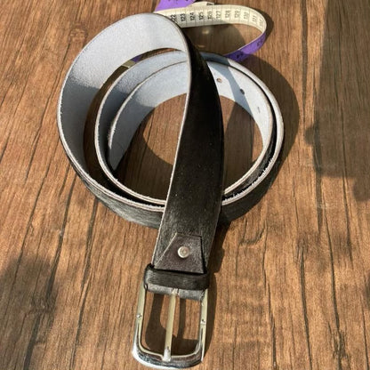 A dark brown leather belt with a silver-tone metal buckle, coiled on a wooden surface.