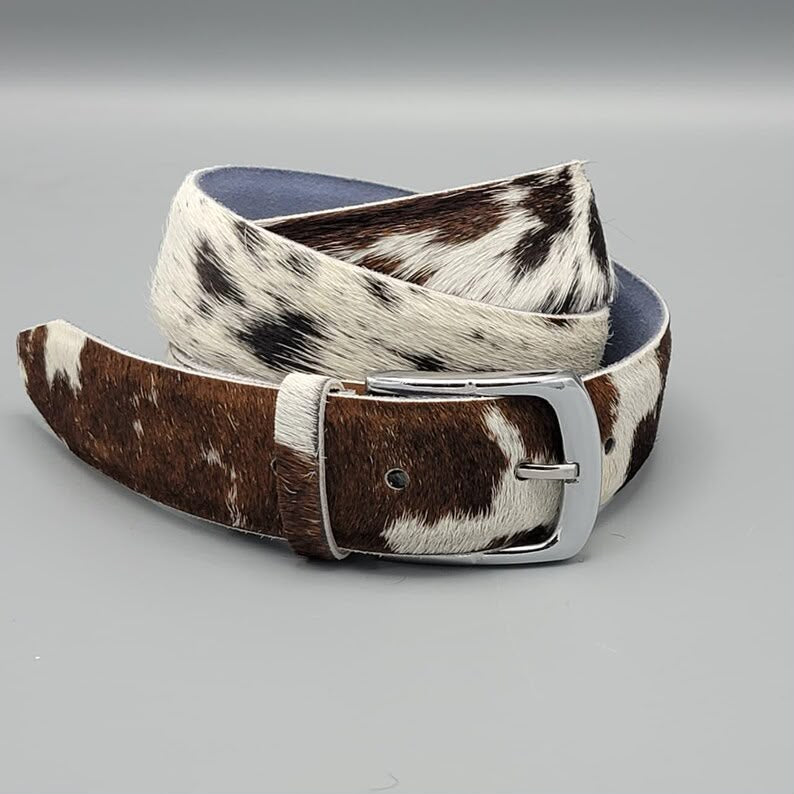 Brown and white cowhide belt with a silver buckle on a gray background