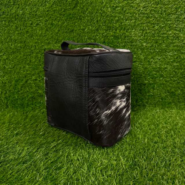 A black insulated cooler bag with a black-and-white cowhide patterned front panel and top, standing on green artificial grass.