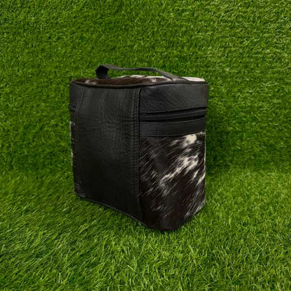 A black insulated cooler bag with a black-and-white cowhide patterned front panel and top, standing on green artificial grass.