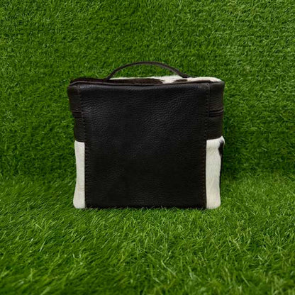 A small rectangular handbag or pouch made of black pebbled leather with white cowhide side panels and a dark handle, photographed against a green grass-like background.