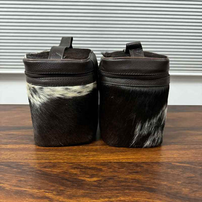 Two dark brown leather zippered pouches with black and white cowhide lower sections, displayed side-by-side on a wooden table.