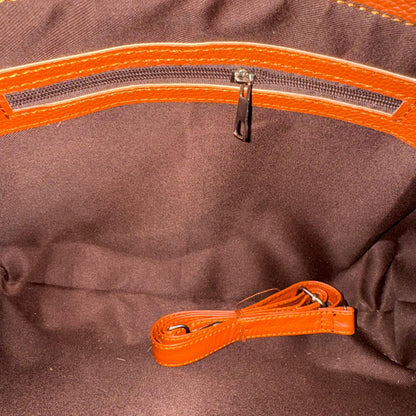 Close-up of the interior of a brown fabric bag or tote, showing an orange zipper trim and a matching orange detachable strap coiled at the bottom.