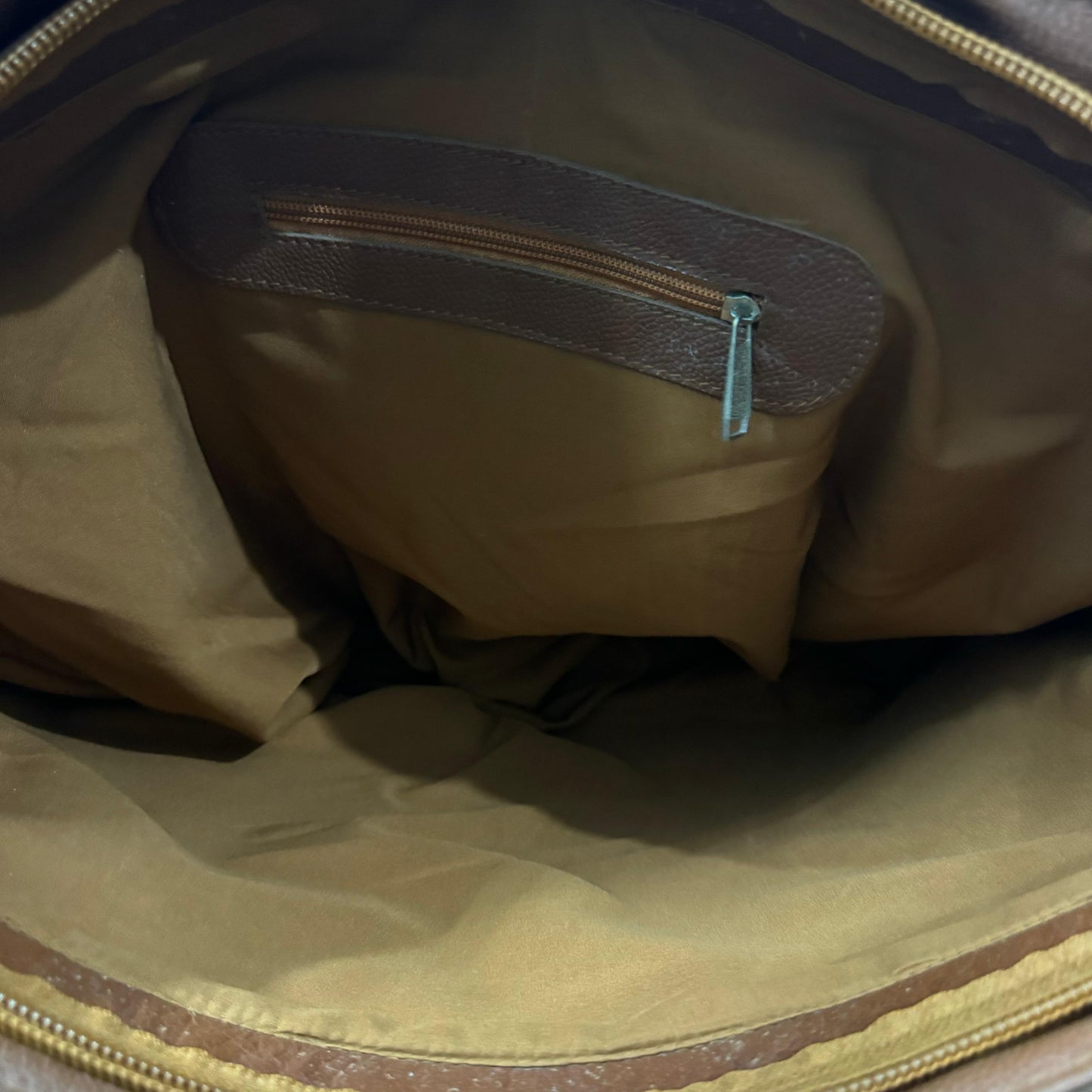 Close-up view of the interior of a brown and tan bag, showing a tan nylon main body, a brown leatherette zippered pocket, and gold-toned metal zippers.