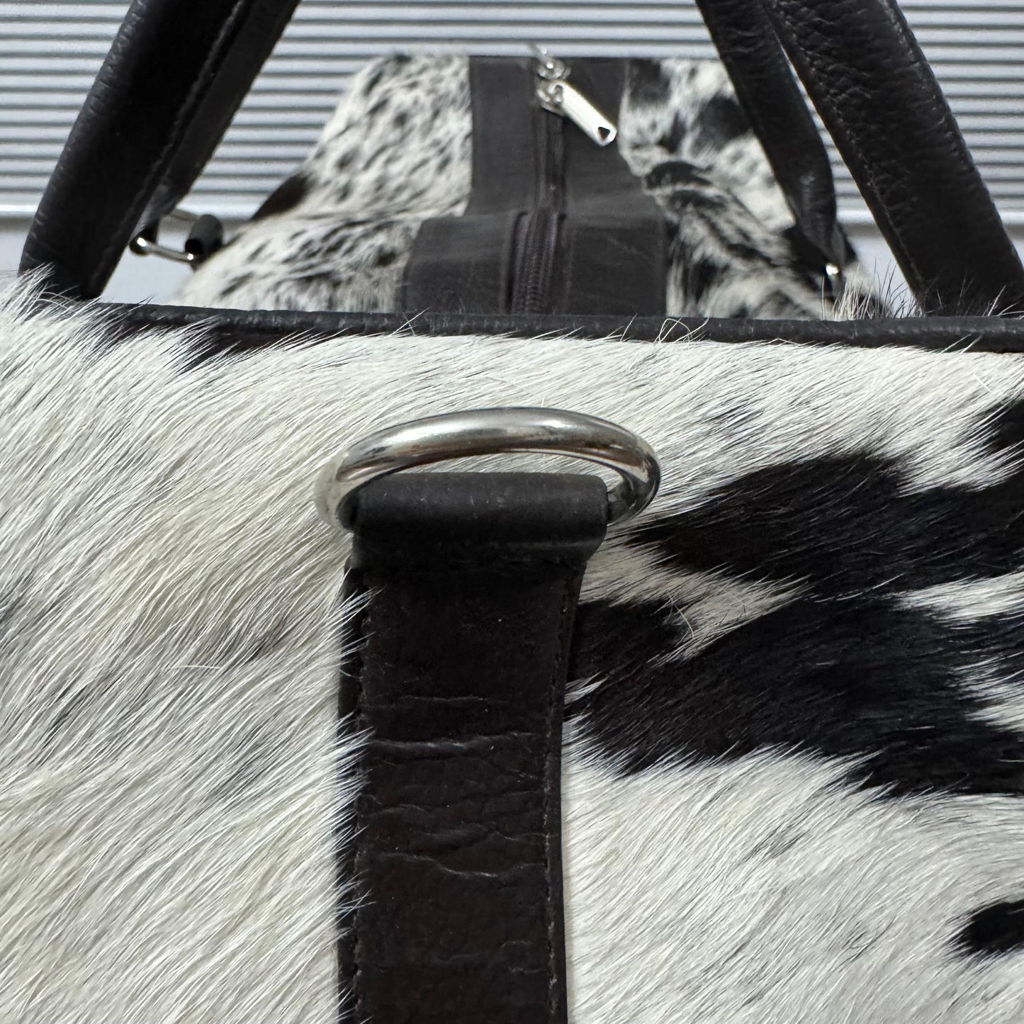 Close-up of a black and white cowhide bag with black faux-leather trim and a silver metal D-ring closure.