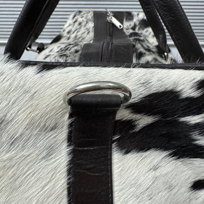 Close-up of a black and white cowhide bag with black faux-leather trim and a silver metal D-ring closure.