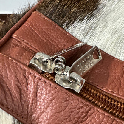 Close-up of a brown textured leather zipper pouch with a silver metal zipper pull, resting on a brown and white fur surface.
