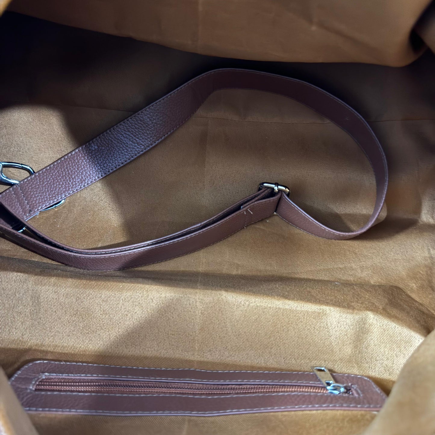 Close-up of a brown leather shoulder strap laid across the inside of a tan fabric bag, with a matching zippered pocket visible along the bottom edge.