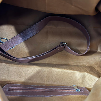 Close-up of a brown leather shoulder strap laid across the inside of a tan fabric bag, with a matching zippered pocket visible along the bottom edge.