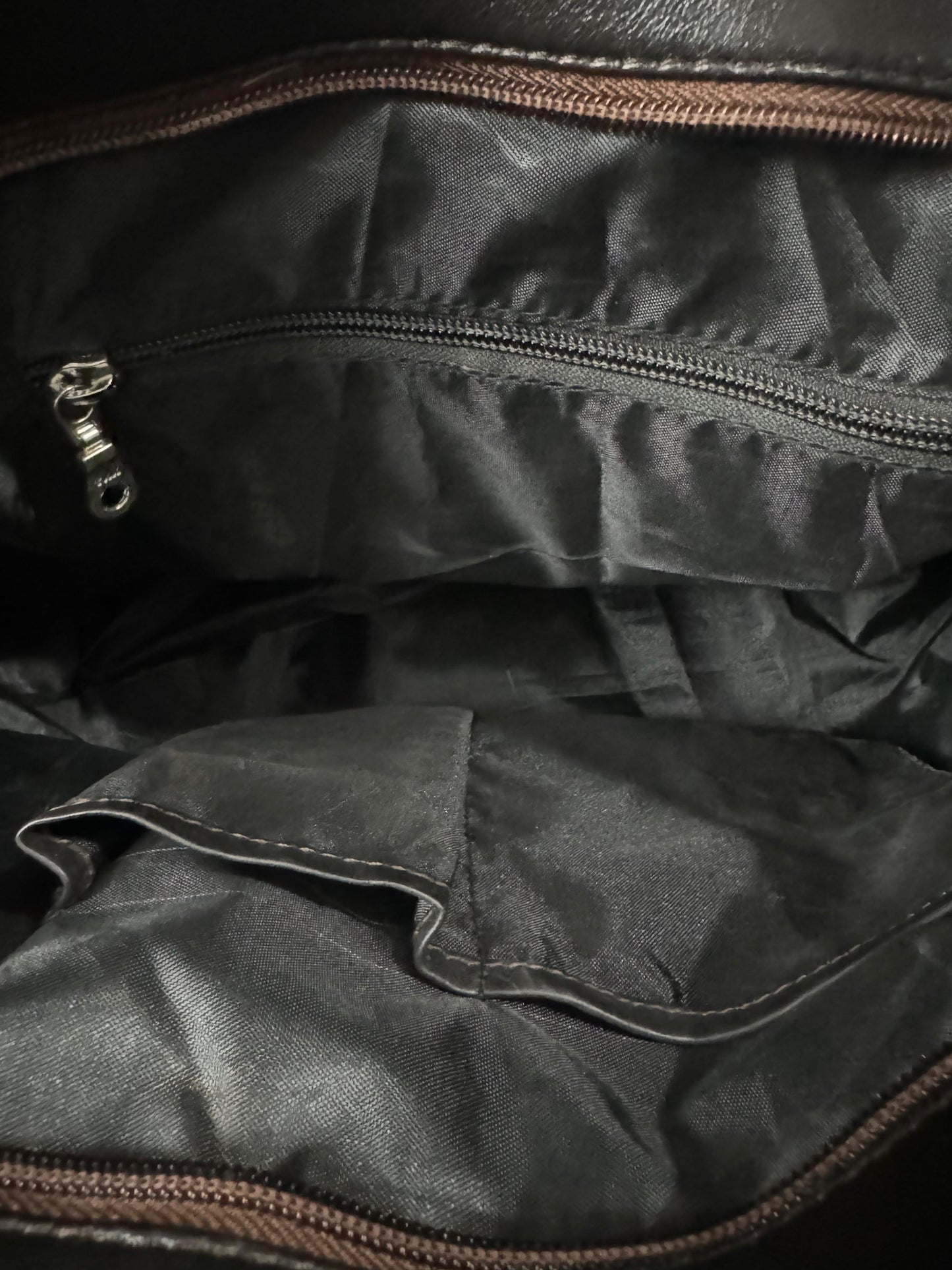 Close-up of the interior of cowhide tote bag, showing a zippered compartment with a silver zipper pull and a pocket with brown zipper trim.