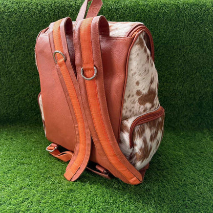 A brown leather and cowhide backpack standing upright on artificial green grass.