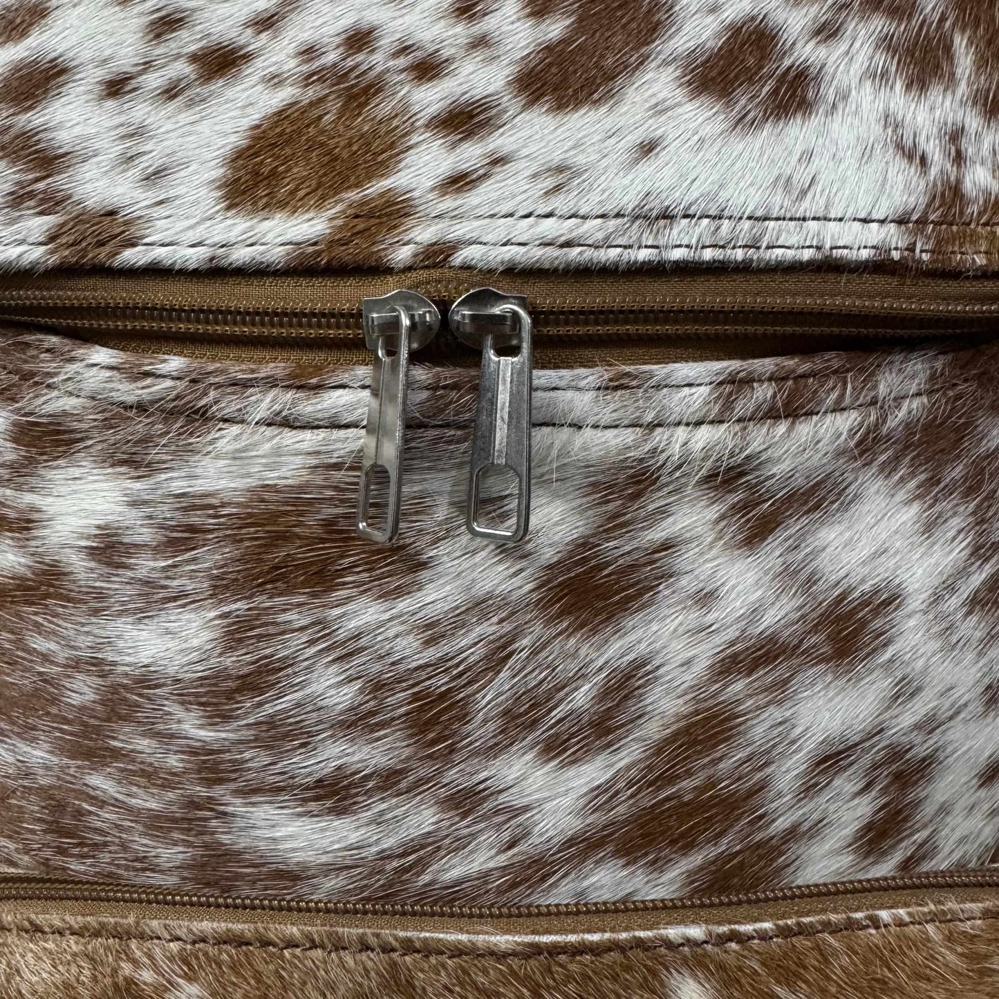 Close-up of a brown and white cowhide-patterned zipper pouch with silver metal zipper pulls.