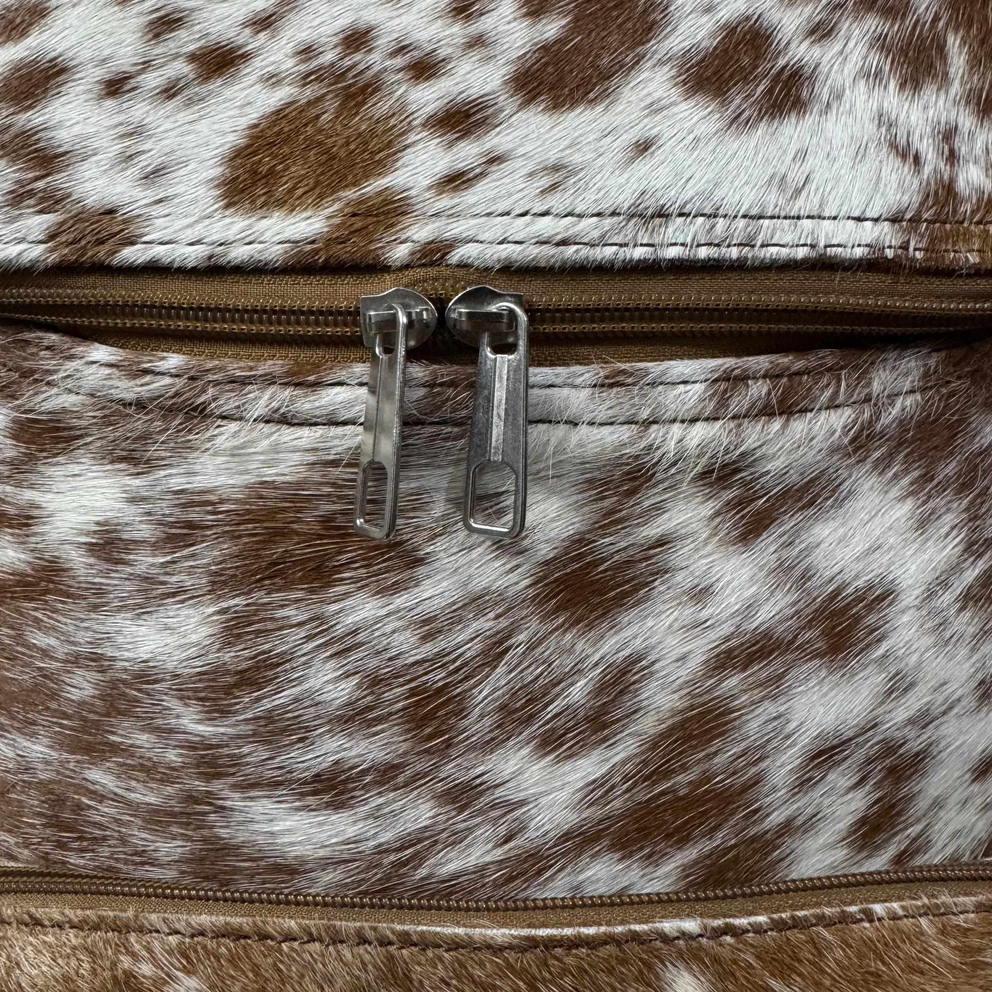 Close-up of a brown and white cowhide-patterned zipper pouch with silver metal zipper pulls.