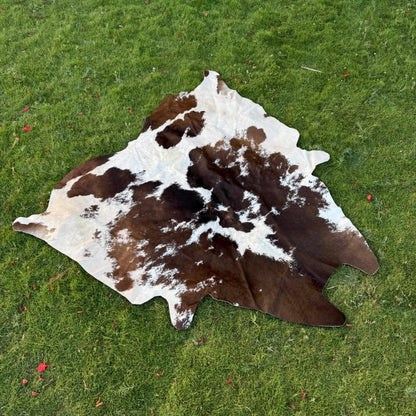 A natural cowhide rug with dark brown and white patches laid out on a green grass lawn.
