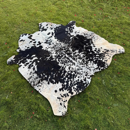 A cowhide rug with a black and white spotted pattern laid out on a green grass lawn.