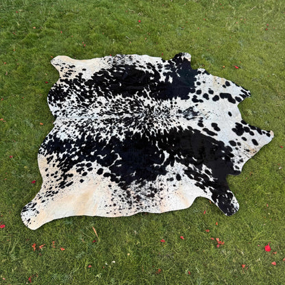 A natural black and white cowhide rug laid flat on a green grass lawn.