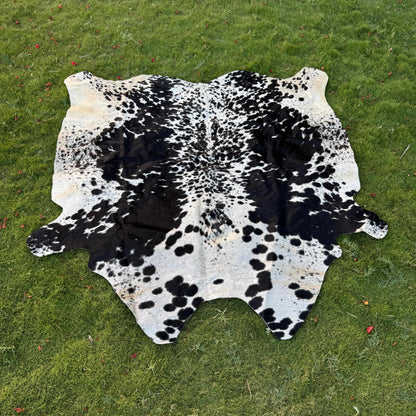 A black and white cowhide rug laid flat on a green grass lawn.