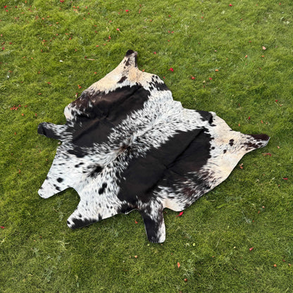 A natural black and white cowhide rug laid flat on a green grass lawn.