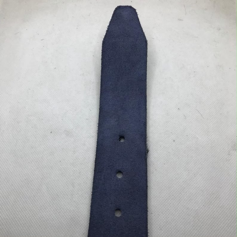 A close-up of a dark navy blue suede or nubuck strap, likely for a watch or accessory, laid vertically on a textured off-white fabric background.