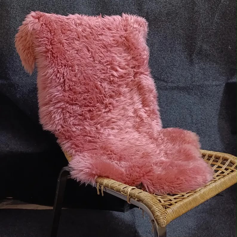 Blush pink sheepskin rug draped over a woven lounge chair