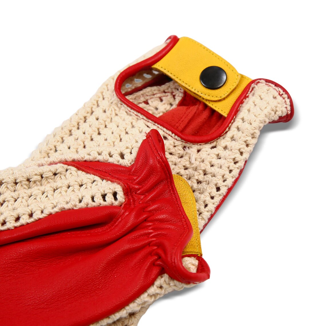 Close-up of a knit glove with beige open-knit fabric, red leather-like sections, and yellow strap accents with a black snap button, shown on a white background.