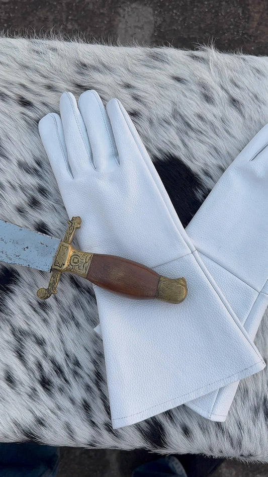 A pair of white leather gloves laid flat on a black-and-white spotted faux fur surface, with a decorative dagger resting across them.