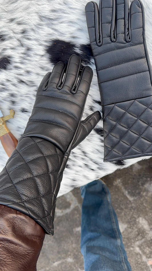 Black quilted leather gloves with touchscreen-compatible fingertips, shown on a person's hand and laid flat on a black-and-white cowhide rug.