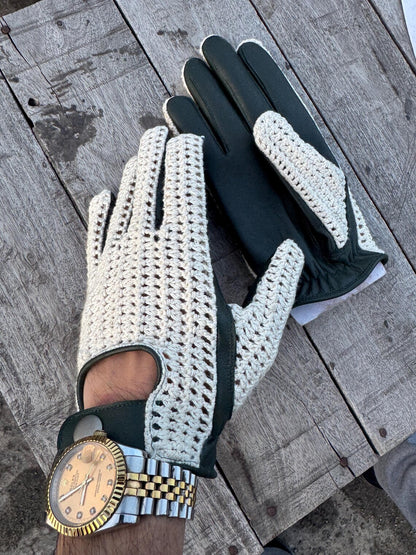 A pair of golf gloves, one cream crocheted with dark green trim and one solid dark green, shown on a person's hands resting on a weathered wooden surface.