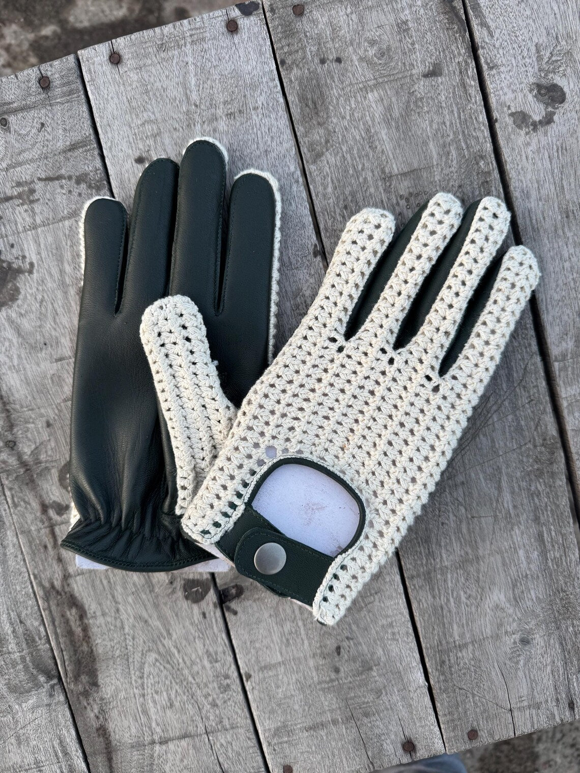 A pair of golf gloves laid flat on weathered gray wooden planks. One glove is solid black, and the other is off-white with a black palm and black finger sections.