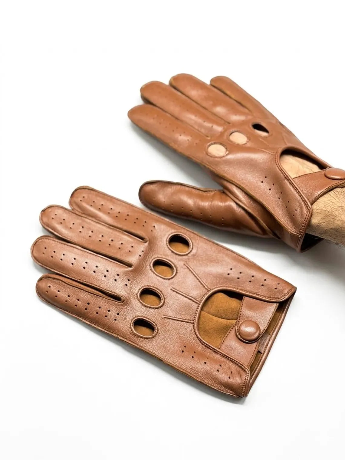 A pair of brown leather driving gloves with perforated ventilation holes and button closures, displayed on a clean white background.