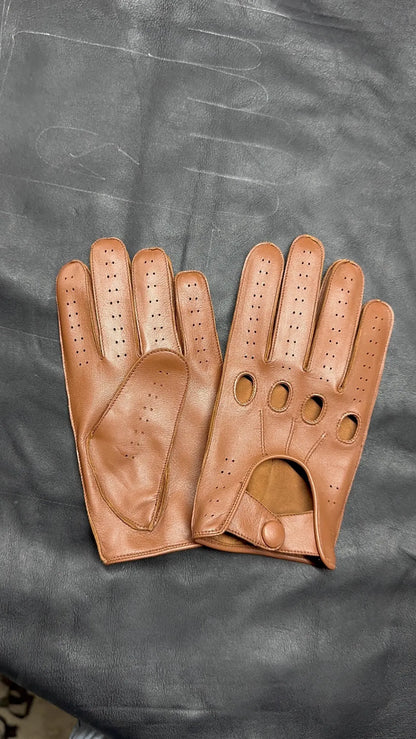 A pair of tan leather driving gloves with perforated details, displayed flat on a dark gray textured surface.