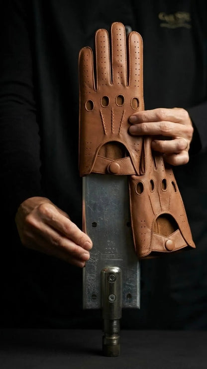 A person wearing a black shirt holds up a pair of brown leather gloves with a unique mechanical design, featuring circular cutouts and a metal bar attached to the back of each glove.