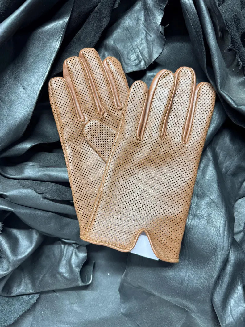 A pair of tan perforated leather gloves laid flat on a dark gray and black draped fabric background.