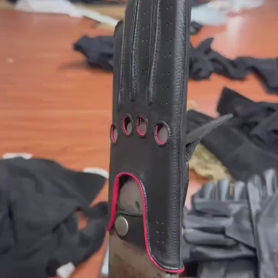video of A pair of black leather golf gloves with red trim and ventilation perforations, .