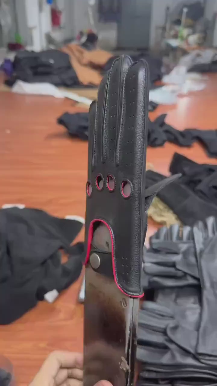 video of A pair of black leather golf gloves with red trim and ventilation perforations, .