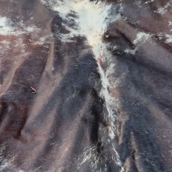 A natural black and white cowhide rug laid flat on a green grass lawn.