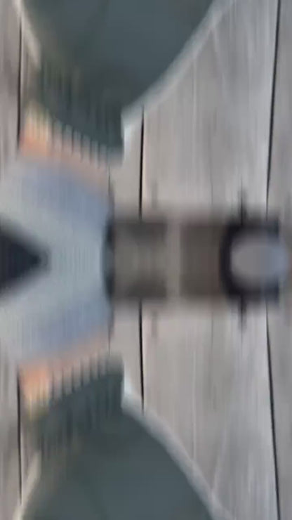 video of A pair of dark green leather gloves with white knit trim and textured white grip panels on the palms, shown being worn with a gray knit cuff and black jacket sleeve against a cobblestone pavement background.