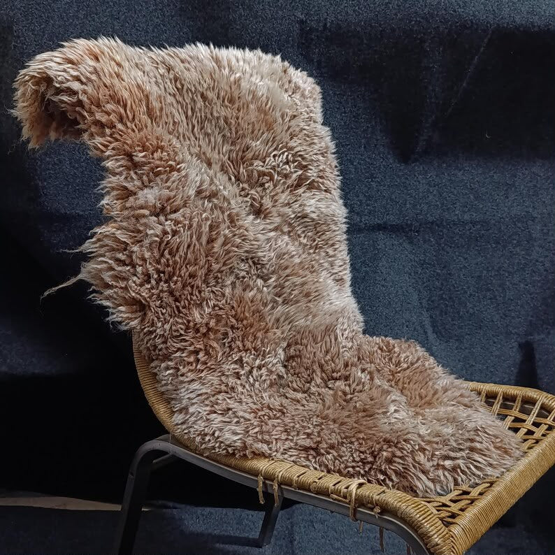 Sandy brown sheepskin rug draped over a woven lounge chair