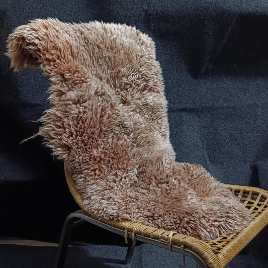 Sandy brown sheepskin rug draped over a woven lounge chair