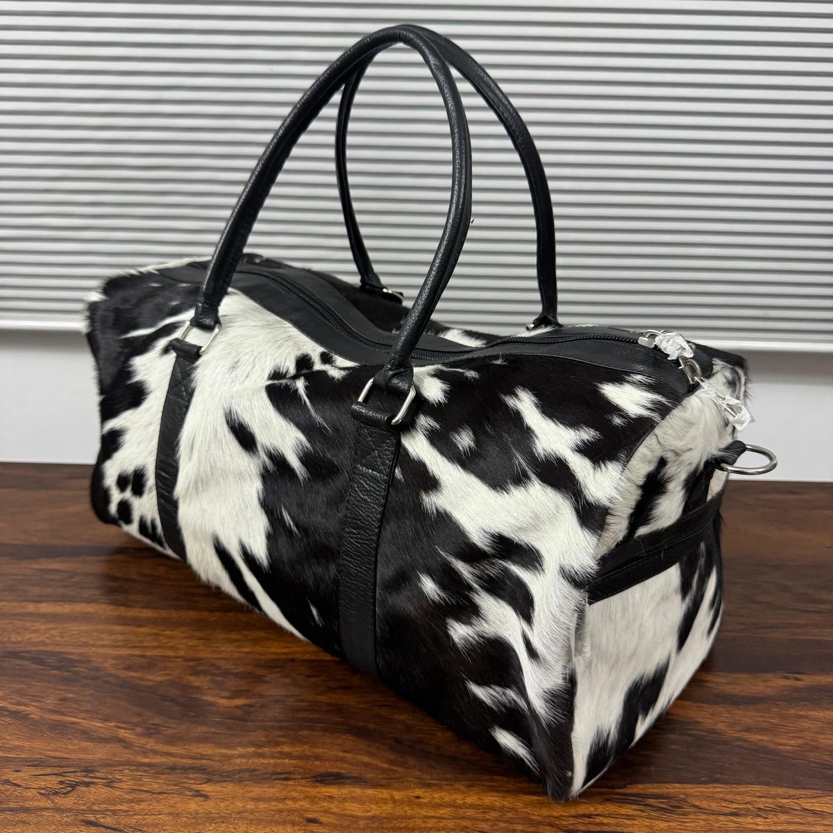 Spotted cowhide duffel bag showing side compartments and handles