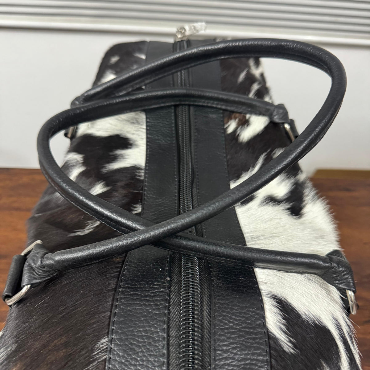 Top zipper and handles on black and white cowhide duffel bag