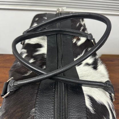 Top zipper and handles on black and white cowhide duffel bag