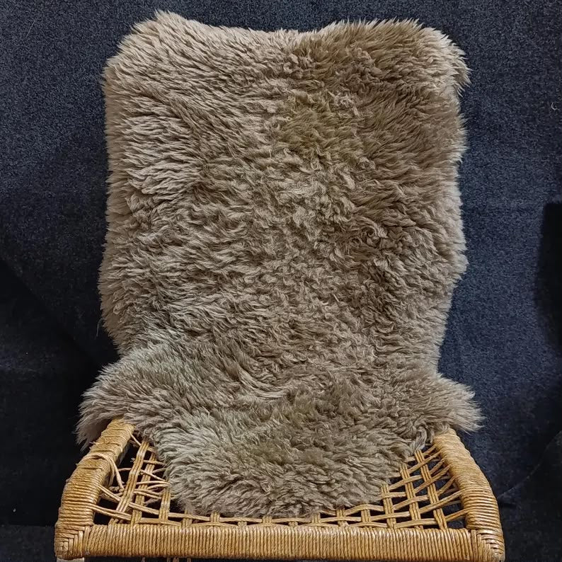 Taupe natural sheepskin rug draped over a lounge chair in a neutral living room